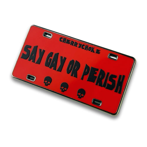 Red “Say Gay or Perish” license plate-inspired enamel pin with black lettering and three skulls, by Cherrychoke.